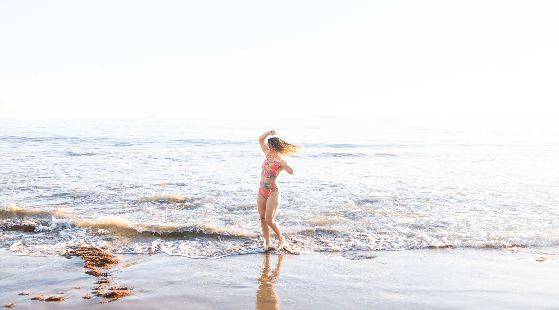 Photo of a woman being carefree and moving around on the beach with the water at her feet.