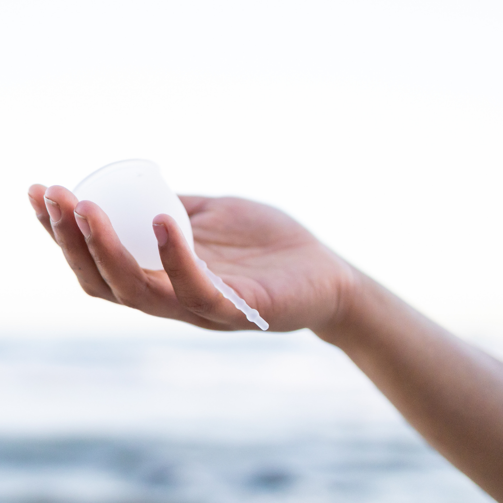 Hand holding clear Kind Cup size regular with ocean in the distance